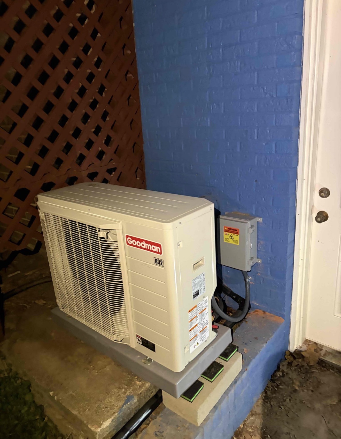 Brand new Goodman R32 condenser installed on a proper composite equipment pad with anti-vibration isolation pads, dedicated electrical disconnect box mounted at correct height